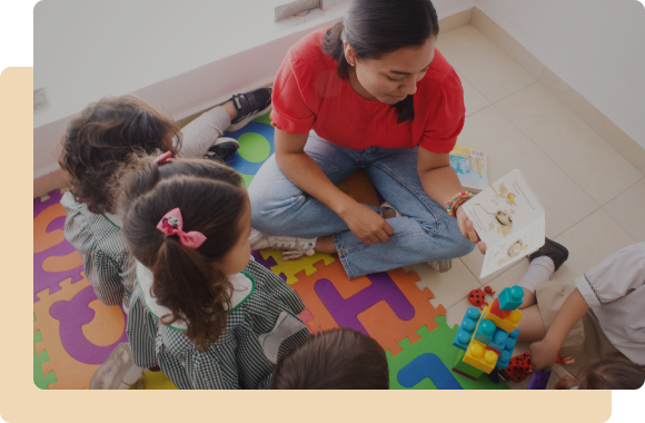 Maestra sentada en el piso enseñando un libro a sus alumnos pequeños